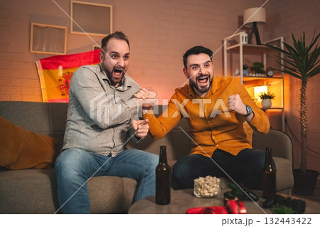 Celebration of friendship and excitement during a sports event in a cozy living room with snacks and drinks Celebration of friendship and excitement during a sports event in a cozy living room with snacks and drinks 132443422