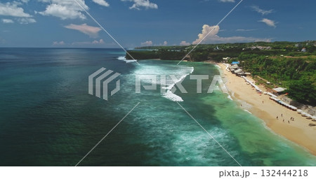Stunning aerial view of Dreamland Beach in Bali, Indonesia, featuring vibrant turquoise waters, gentle waves on white sand, and lush green cliffs under a bright blue sky Stunning aerial view of Dreamland Beach in Bali, Indonesia, featuring vibrant turquoise waters, gentle waves on white sand, and lush green cliffs under a bright blue sky 132444218
