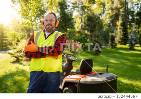 Gardener standing in sunny garden with lawnmower surrounded by green plants Gardener standing in sunny garden with lawnmower surrounded by green plants 132444667