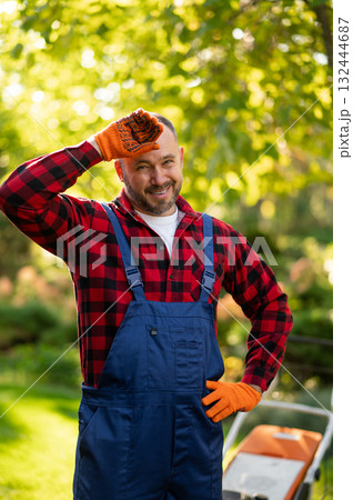Professional gardener with protective gloves and goggles posing beside lawn cutting machine Professional gardener with protective gloves and goggles posing beside lawn cutting machine 132444687