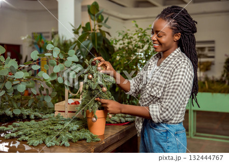 Female flower shop assistant decorating small christmas tree and looking involved 132444767
