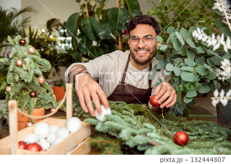 Positive man decorating christmas tree branches with red balls and feeling joyful 132444807