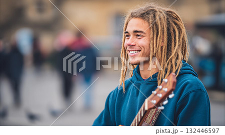 Young musician smiles while playing guitar outdoors in a crowded square surrounded by people enjoying the day 132446597