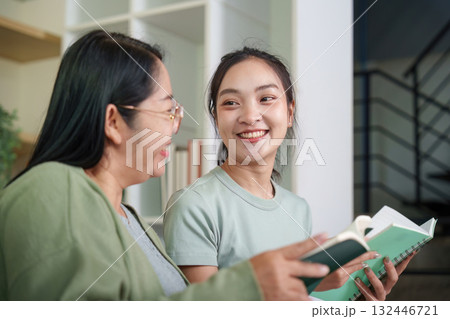 Mother and daughter sharing smiles while reading together 132446721