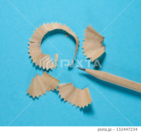 A wooden pencil and several neat curls of pencil shavings on a blue background 132447234
