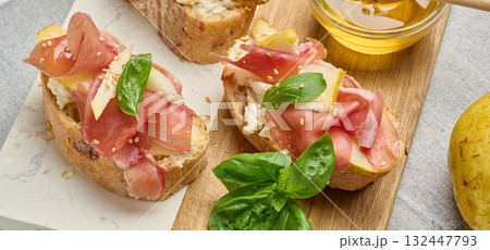 Italian bruschetta with prosciutto, pear, soft cheese, honey and sesame seeds. Italian bruschetta with prosciutto, pear, soft cheese, honey and sesame seeds. 132447793