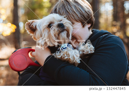 Adorable yorkshire terrier dog being held by a happy pet owner in the autumnal forest. A cute doggy on the hands of a woman. Real emotions of love. 132447845
