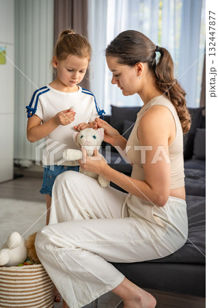 Mother and daughter repairing an old plush toy together. Sustainable lifestyle, mindful consumption, and conscious parenting at home 132447877