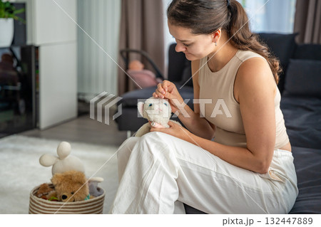 Young woman sewing an old plush toy at home with needle and thread. Sustainable lifestyle and conscious consumption as part of eco friendly and mindful living. 132447889