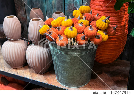 Mini velvet pumpkins in warm orange and yellow tones arranged in a rustic metal bucket. Thanksgiving crafts, cozy seasonal decor, soft sculpture accents, autumn home styling 132447919