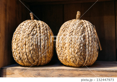 Two decorative pumpkins made from braided natural straw displayed on a wooden shelf. Reusable seasonal decor, zero-waste styling, handcrafted home accents, eco-friendly holiday alternatives Two decorative pumpkins made from braided natural straw displayed on a wooden shelf. Reusable seasonal decor, zero-waste styling, handcrafted home accents, eco-friendly holiday alternatives 132447973