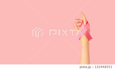 International symbol of Breast Cancer Awareness Month in October. Close up of female hand holding satin pink ribbon awareness on pink background. Women's health care and medical concept. International symbol of Breast Cancer Awareness Month in October. Close up of female hand holding satin pink ribbon awareness on pink background. Women's health care and medical concept. 132448551