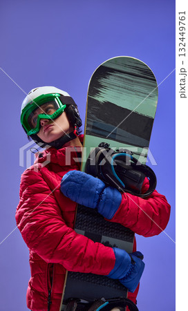 Snowboarder in red jacket hugging snowboard wearing green goggles and blue gloves 132449761