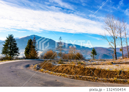 country road in carpathian mountains. beautiful landscape of ukraine in late autumn. fir trees on the roadside in morning light. scenic view of blue sky with clouds above the distant ridge in snow 132450454