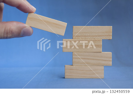 Hand preparing to place wooden block on lower stack showing teamwork and foundation concept with customizable space for text or ideas. Hand preparing to place wooden block on lower stack showing teamwork and foundation concept with customizable space for text or ideas. 132450559