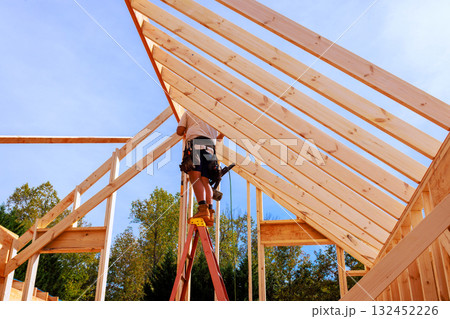 Worker climbs ladder to secure wooden beams for house under assembly together Worker climbs ladder to secure wooden beams for house under assembly together 132452226