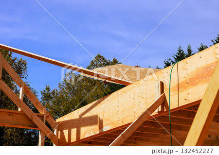 Construction workers install roof materials on wooden beams frame in suburban neighborhood Construction workers install roof materials on wooden beams frame in suburban neighborhood 132452227