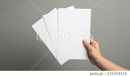 Hand holding three blank white flyers against a gray background Hand holding three blank white flyers against a gray background 132454310