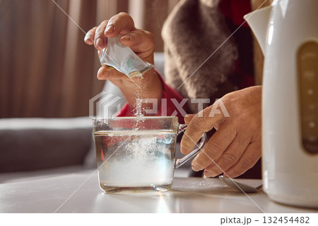 Senior woman dissolving powdered medicine in glass mug with hot water 132454482