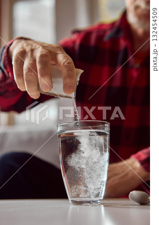 Older man adding medicine powder into glass of water during home treatment Older man adding medicine powder into glass of water during home treatment 132454509