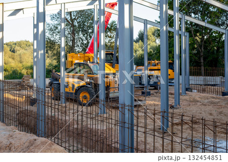 Orange telescopic handlers and a mobile crane at the construction site of a building under construction. 132454851
