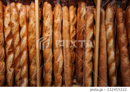 Row of bread loaves are displayed in a wooden case. The loaves are all brown and appear to be freshly baked. 132455222