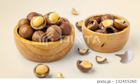 Macadamia nuts with shell in wooden bowls with broken macadamia and tool on beige background Macadamia nuts with shell in wooden bowls with broken macadamia and tool on beige background 132455260