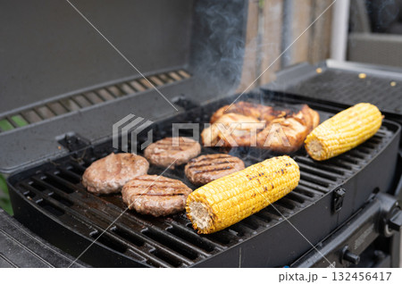 Grilled corn, chicken, and burgers cooking on a backyard bbq grill 132456417