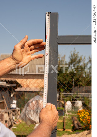 Adult male measuring metal fence with tape measure in garden setting Adult male measuring metal fence with tape measure in garden setting 132456447