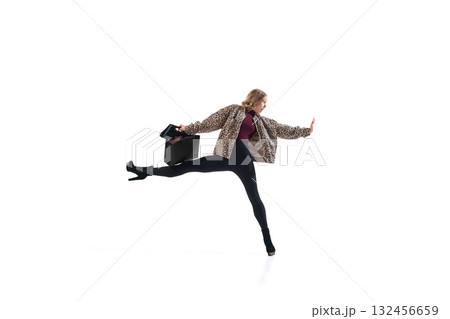 Fashion model in leopard jacket stretching leg while holding shopping bag in expressive pose 132456659