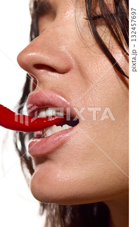 Close-up side view woman biting chili pepper with glowing lips and clean skin Close-up side view woman biting chili pepper with glowing lips and clean skin 132457697