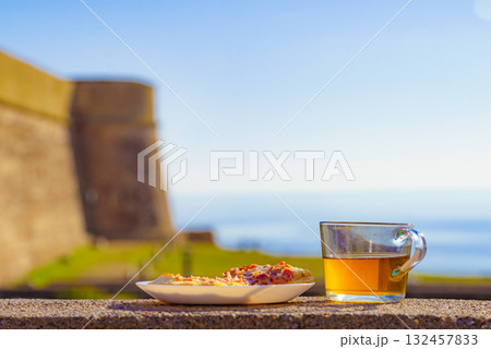 Tea mug and pizza slices on plate, outdoors Tea mug and pizza slices on plate, outdoors 132457833