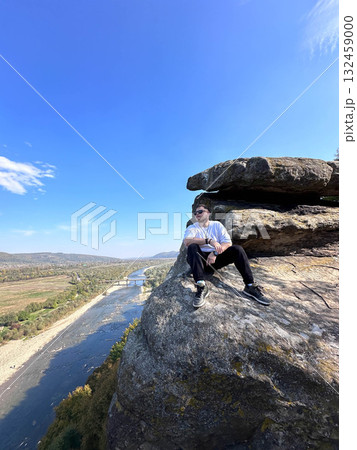 Man Sitting on Cliff Overlooking River and Valley Man Sitting on Cliff Overlooking River and Valley 132459000
