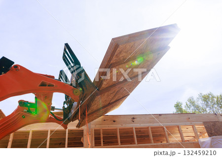 Piece of construction machinery elevates wooden OSB plywood on building site under assembly works Piece of construction machinery elevates wooden OSB plywood on building site under assembly works 132459210