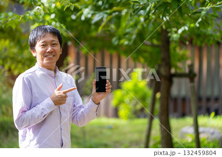 スマホの画面を指差して紹介する笑顔の男性、モバイルアプリの紹介イメージ スマホの画面を指差して紹介する笑顔の男性、モバイルアプリの紹介イメージ 132459804