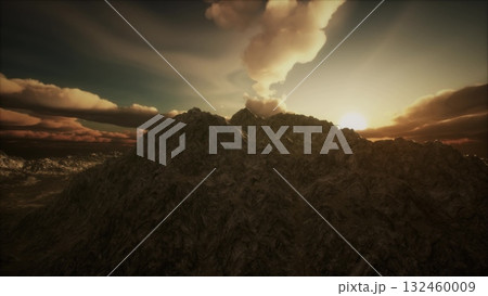 Golden rays of sunlight break through dramatic clouds, illuminating rugged mountain peaks. The tranquil moment captures the raw beauty of nature at dawn, inviting reflection and admiration. 132460009