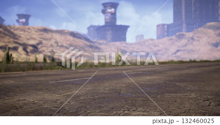 A desolate roadway stretches through a barren landscape where ruins emerge in the distance. Scrub vegetation dots the terrain under a clear blue sky and towering mountains. 132460025