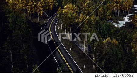 Curving gently, the road invites travelers into a serene landscape where golden and green trees create a stunning autumn tableau. Natures beauty envelops the path inviting exploration. 132460058