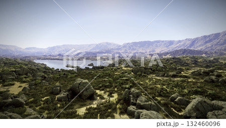 A stunning natural view featuring a tranquil lake nestled among rugged hills and boulders under a clear sky. The vibrant greenery contrasts with the rocky terrain, creating a picturesque setting. 132460096