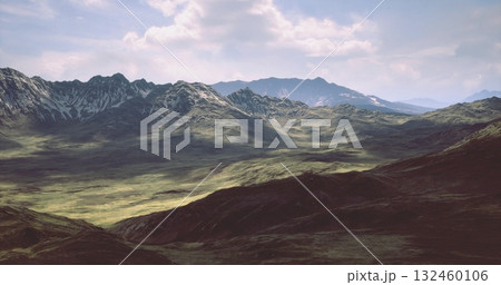 Lush green valleys stretch through a stunning mountain range under a bright sky. Distant peaks are partially covered in snow, showcasing natures grandeur in a serene environment. 132460106