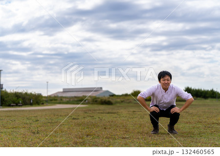 広場で屈伸ストレッチ、芝生でひざを曲げて体をほぐす男性 132460565