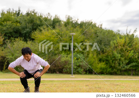 広場で屈伸ストレッチ、芝生でひざを曲げて体をほぐす男性 132460566