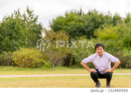 広場で屈伸ストレッチ、芝生でひざを曲げて体をほぐす男性 132460568