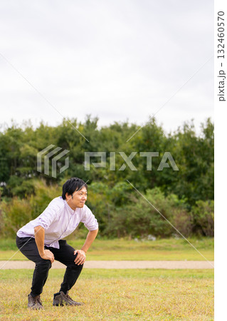 広場で屈伸ストレッチ、芝生でひざを曲げて体をほぐす男性 132460570