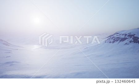 A vast, icy terrain stretches under the gentle glow of the early sun. Snow covered mountains rise in the distance, enveloped in a tranquil and ethereal atmosphere, signaling a new day. 132460645