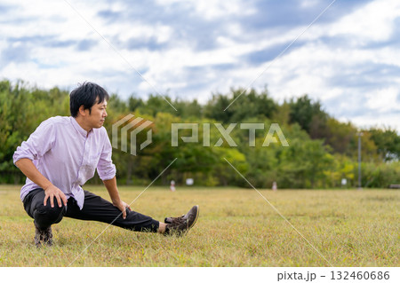 しゃがんで片脚を伸ばす男性のストレッチ｜屋外フィットネス 132460686