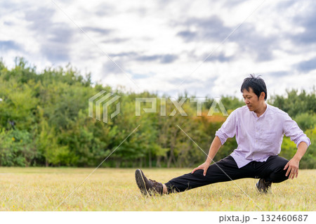 しゃがんで片脚を伸ばす男性のストレッチ｜屋外フィットネス 132460687