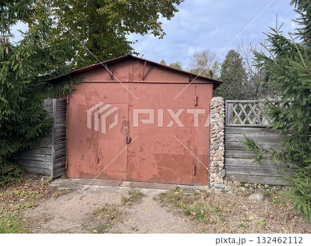 Rustic red shed surrounded by greenery and wooden fence, showcasing a weathered exterior and natural elements, ideal for outdoor storage or garden use 132462112