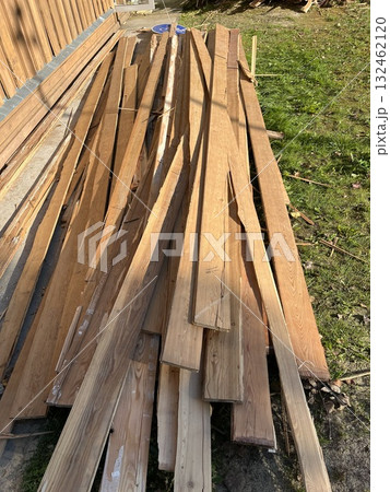 Pile of wooden planks arranged haphazardly on grass, showcasing various textures and colors, ideal for construction or DIY projects with natural materials 132462120