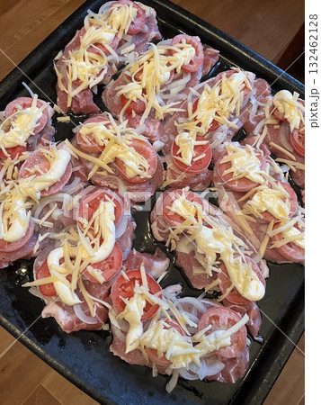 Freshly prepared meat dish topped with sliced tomatoes, shredded cheese, and creamy sauce, arranged on a baking tray ready for cooking, showcasing culinary artistry and delicious flavors 132462128